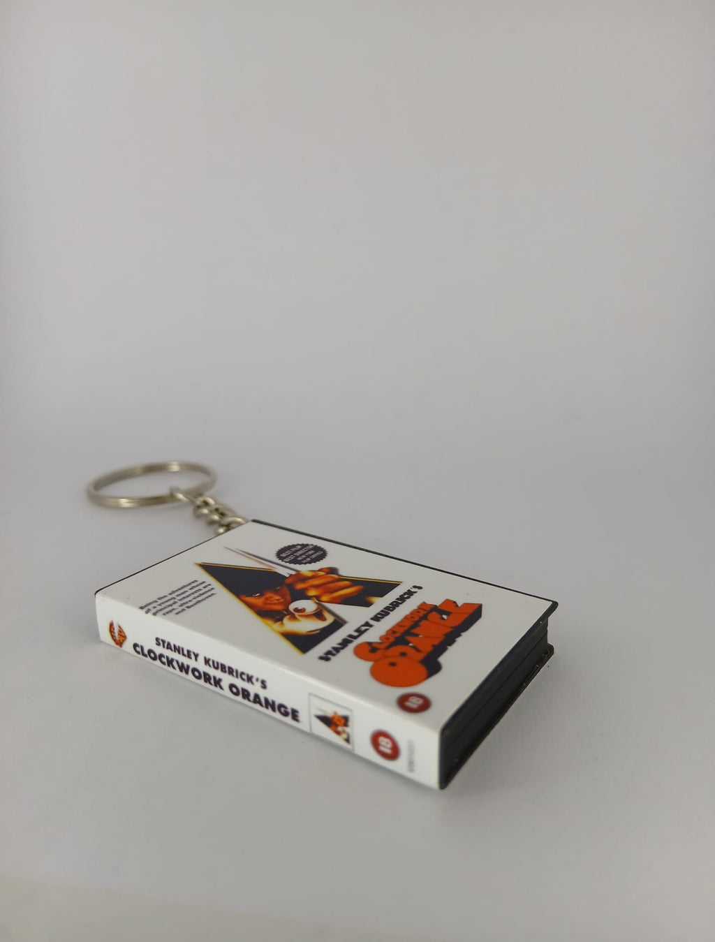 A Clockwork Orange VHS keyring — front cover standing with coin for scale