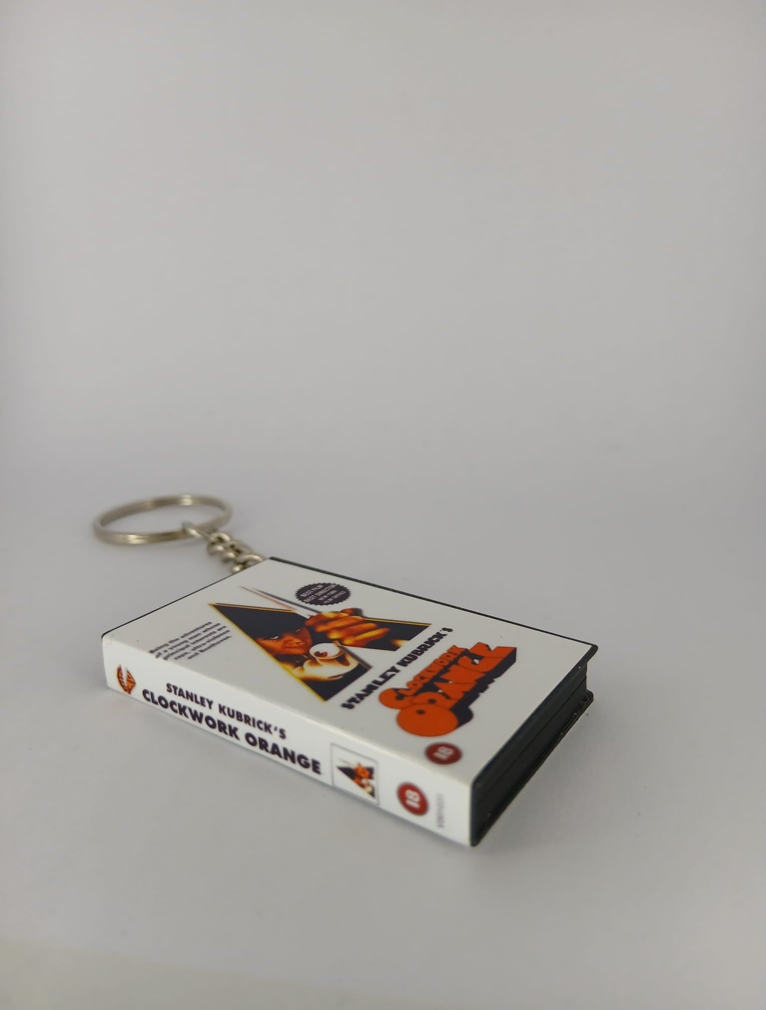 A Clockwork Orange VHS keyring — front cover standing with coin for scale
