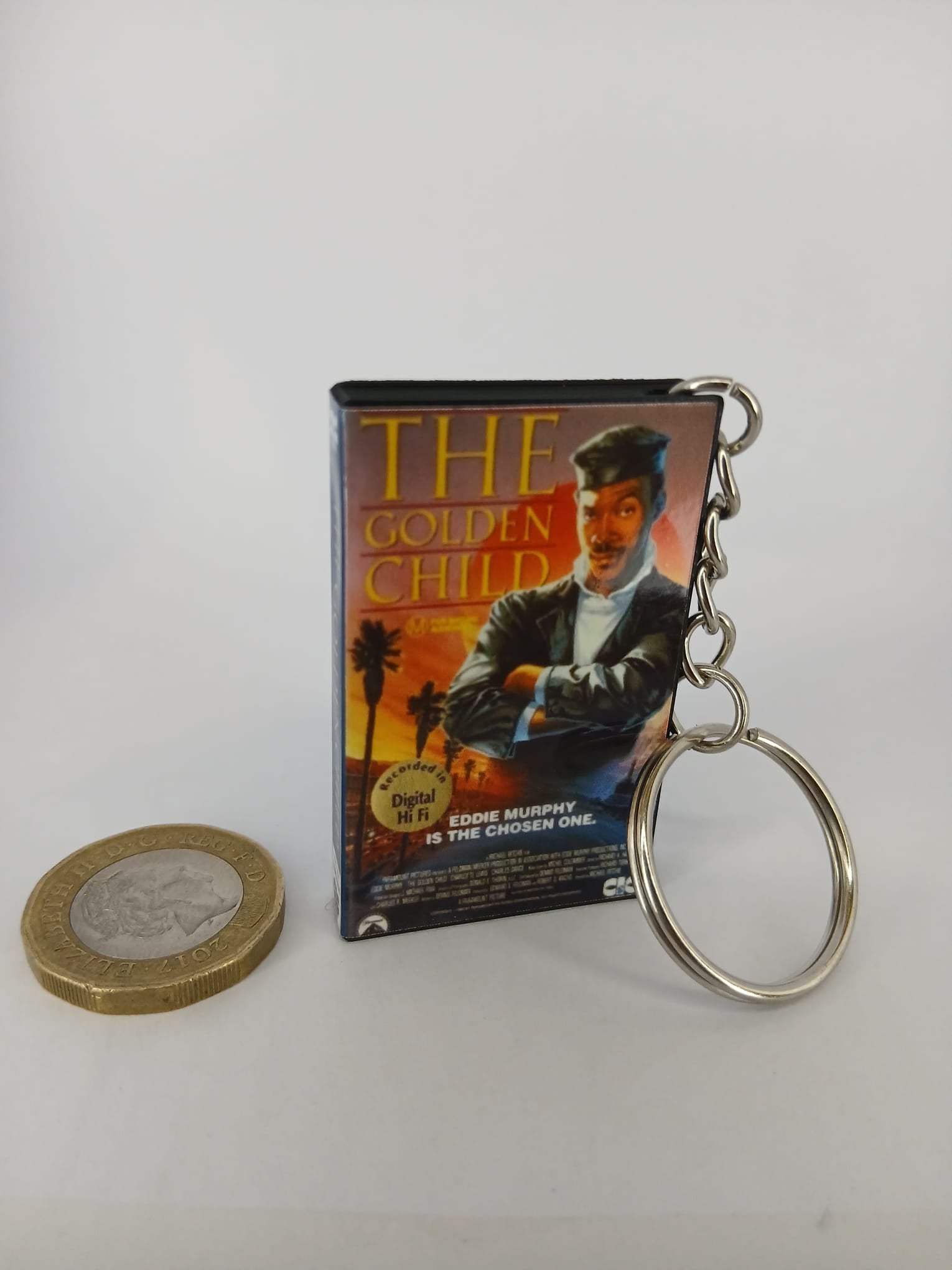 The Golden Child VHS keyring — front cover standing with coin for scale
