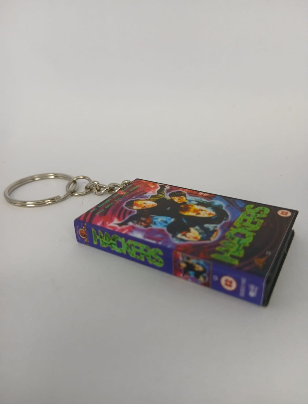 Hackers VHS keyring — front cover standing with coin for scale