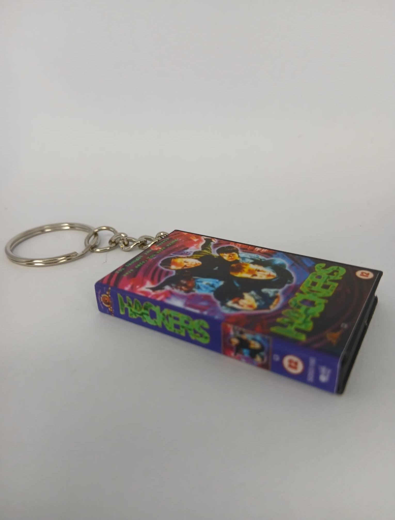 Hackers VHS keyring — front cover standing with coin for scale