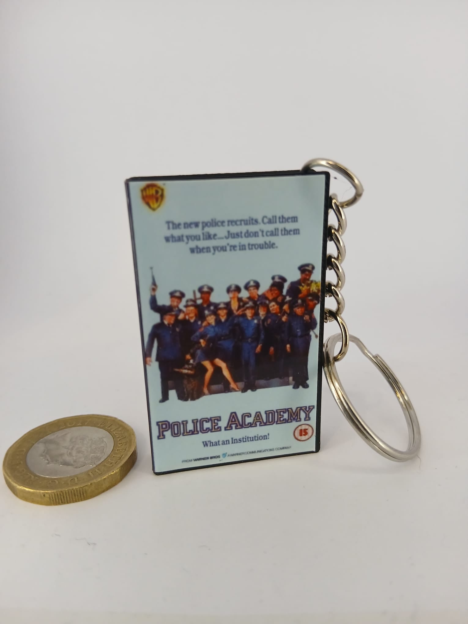 Police Academy VHS keyring — front cover standing with coin for scale