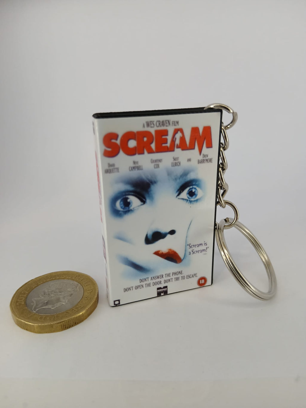 Scream VHS keyring — front cover standing with coin for scale