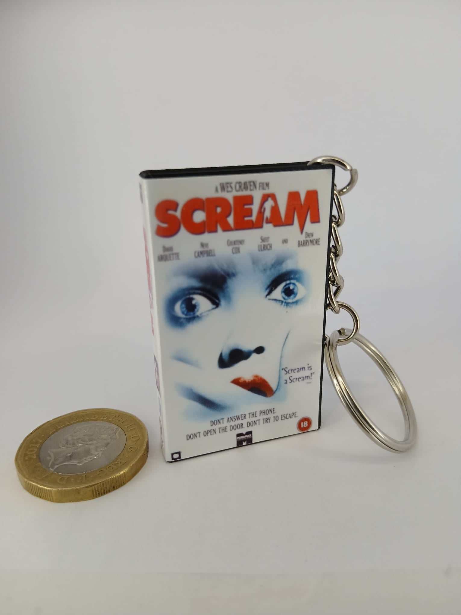 Scream VHS keyring — front cover standing with coin for scale