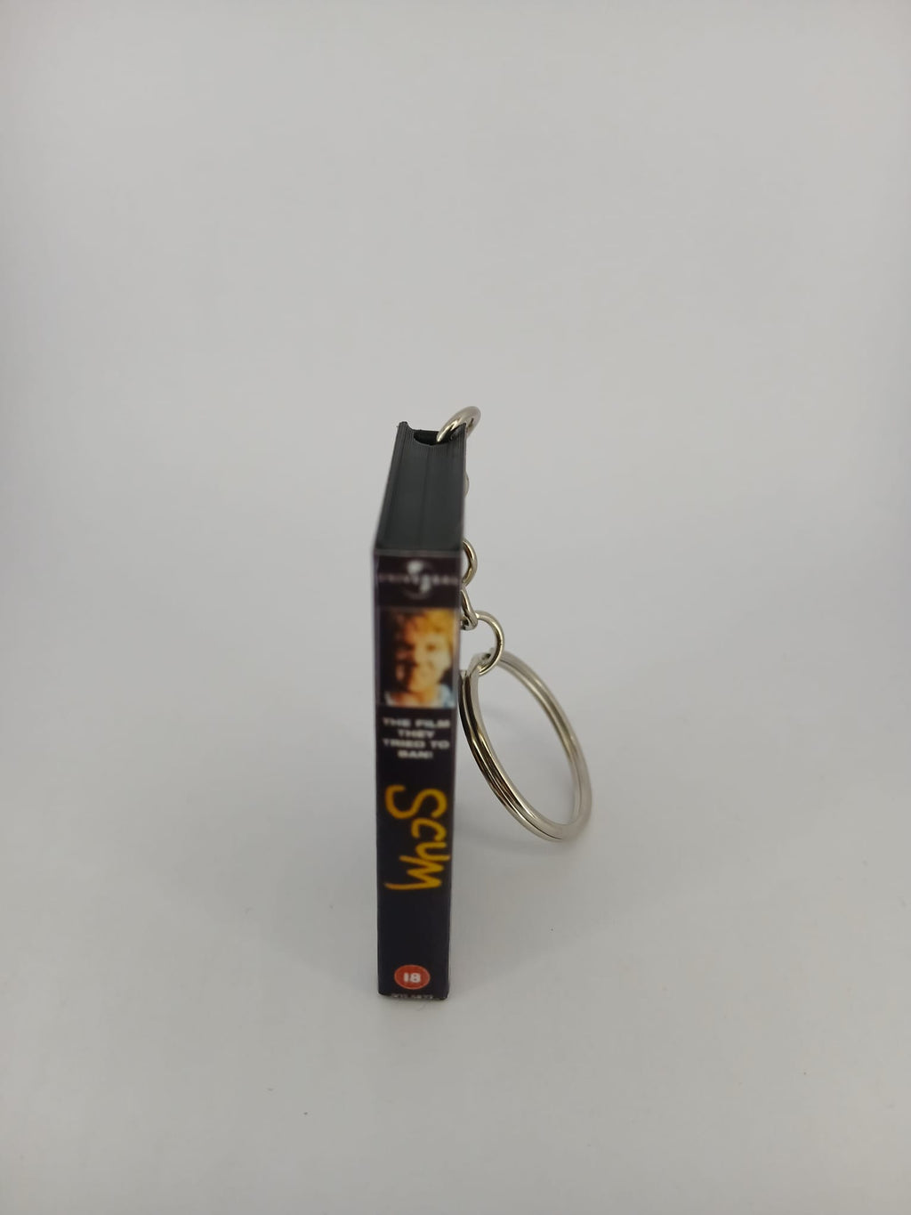Scum VHS keyring — front cover standing with coin for scale