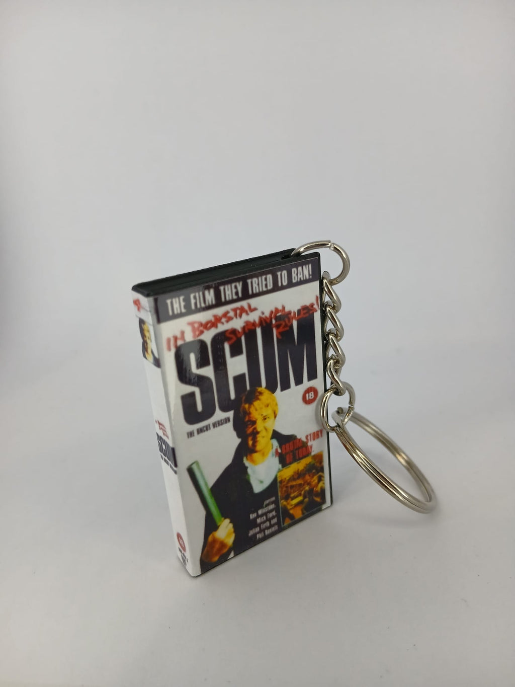 Scum VHS keyring — front cover standing with coin for scale